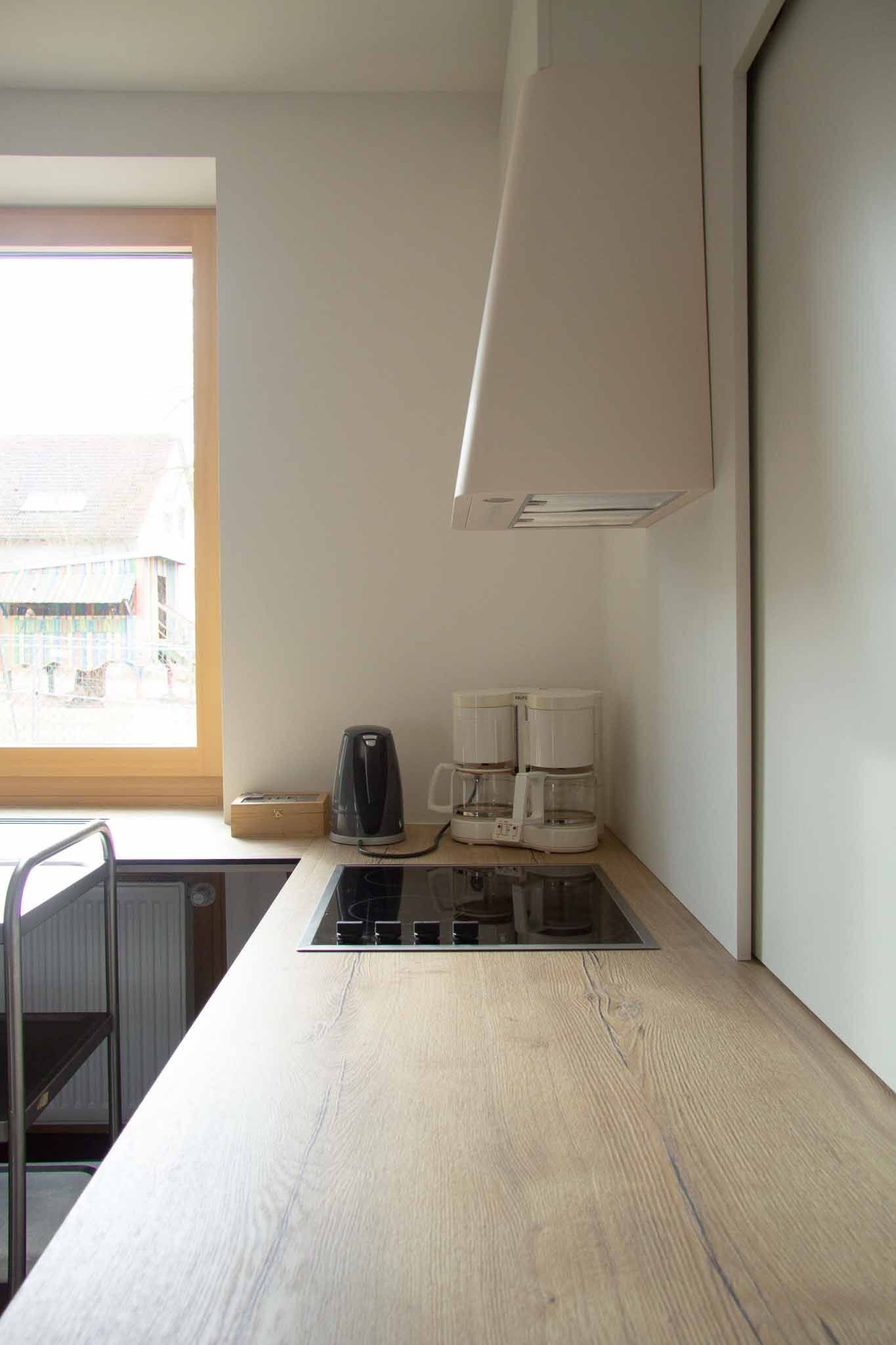 Küchentheke mit Herd, Dunstabzugshaube und Kaffeemaschinen am Fenster.