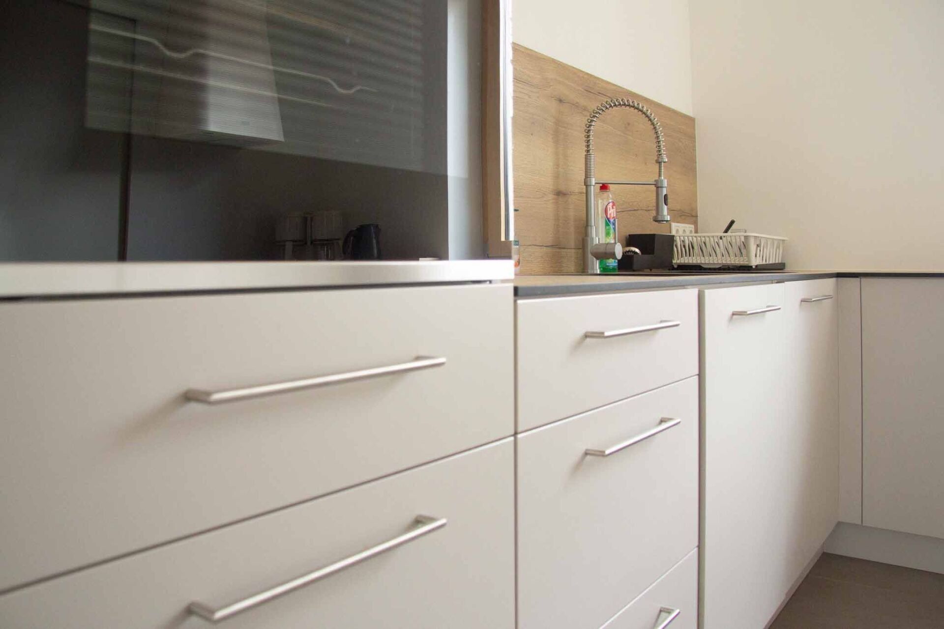 Moderne Küchenschränke mit Edelstahlgriffen; Backofen links, Spüle rechts.