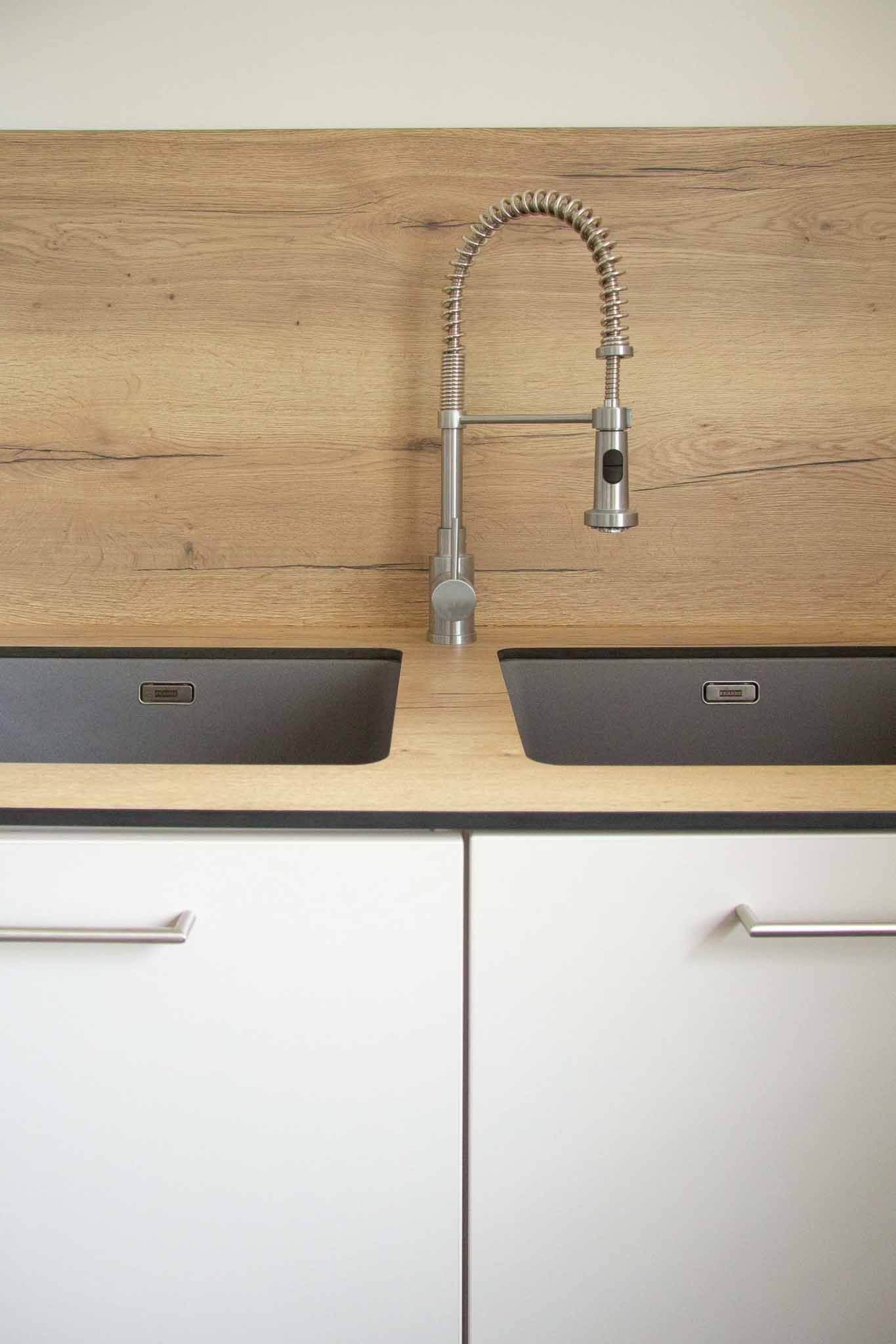 Küchenspüle mit ausziehbarem Wasserhahn, zwei dunkle Spülbecken, weiße Schränke darunter, Küchenrückwand in Holzoptik.