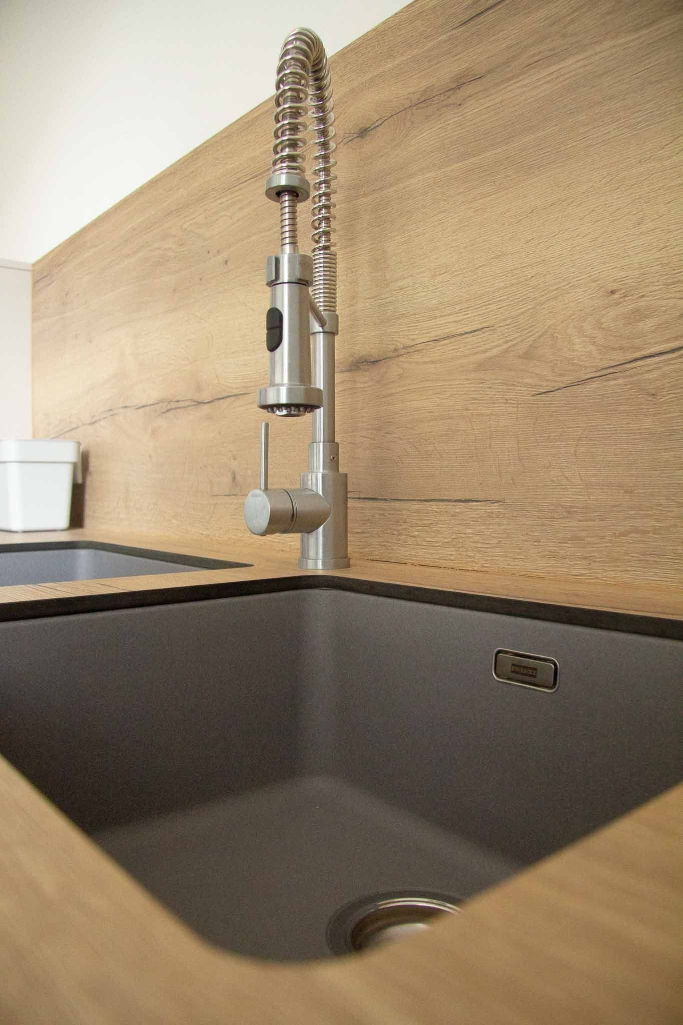 Küchenarmatur aus Edelstahl über einer dunkelgrauen Spüle mit heller Holzverkleidung.