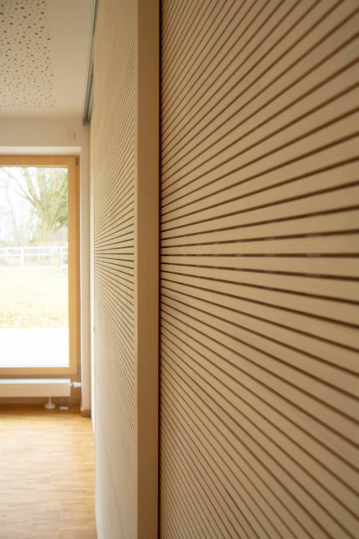 Holzwandpaneele mit horizontalen und wellenförmigen Linien, neben einem Fenster- und Türrahmen.