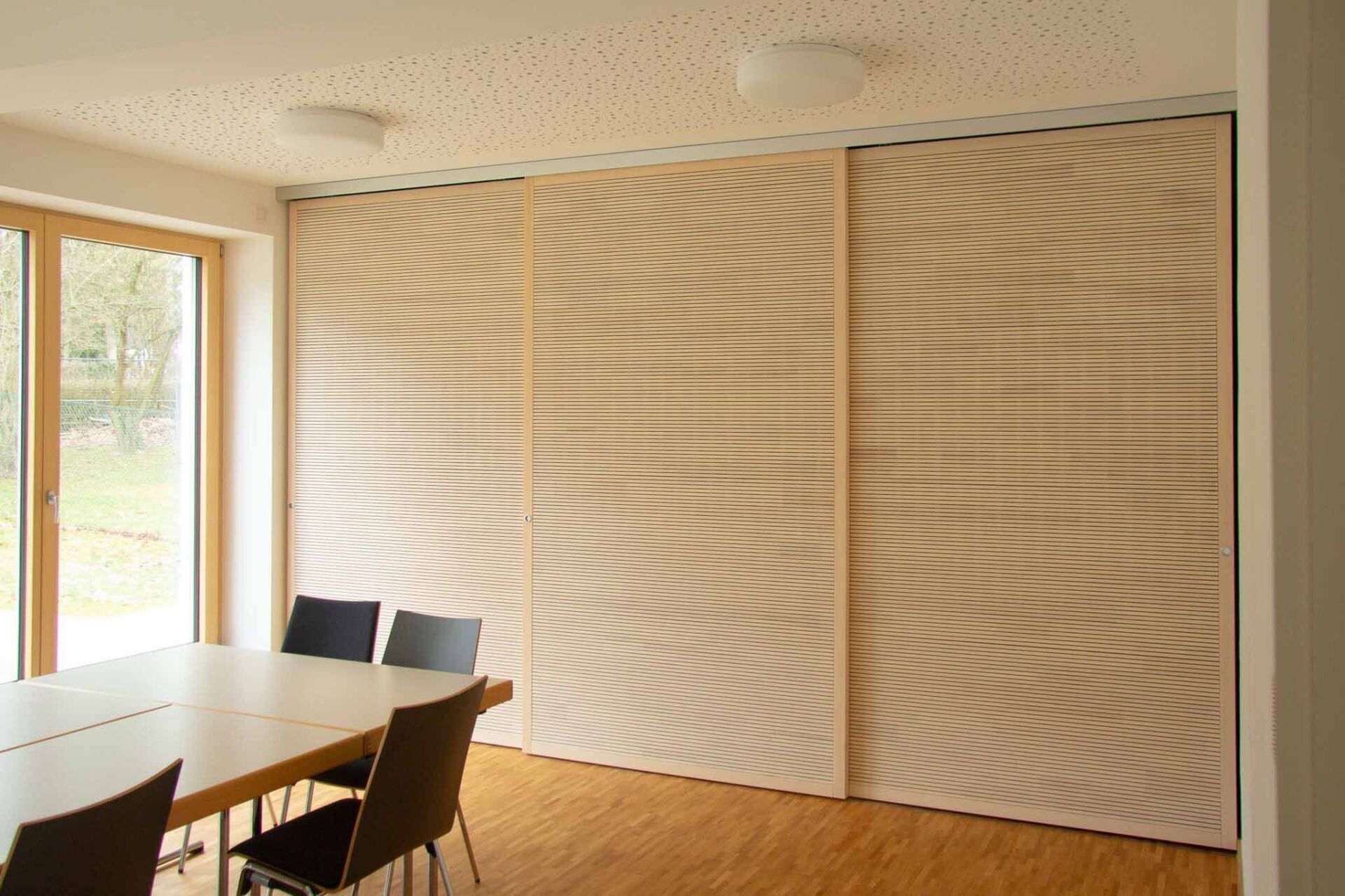 Holzschiebetüren mit Wellenlinien in einem hellen Raum mit Tisch und Stühlen.