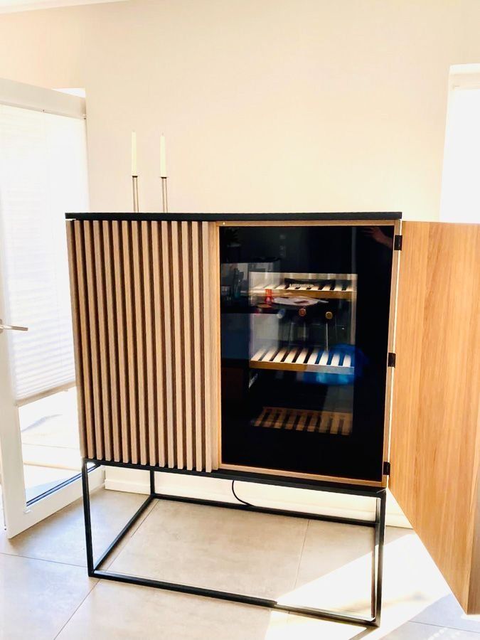 Weinschrank aus Holz mit schwarzem Rahmen, offener Tür und vertikalen Lamellen an der Vorderseite.