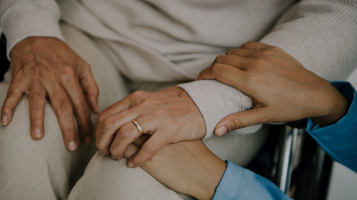 Un cuidador vierte líquido a personas mayores sentadas en una mesa preparada para comer.