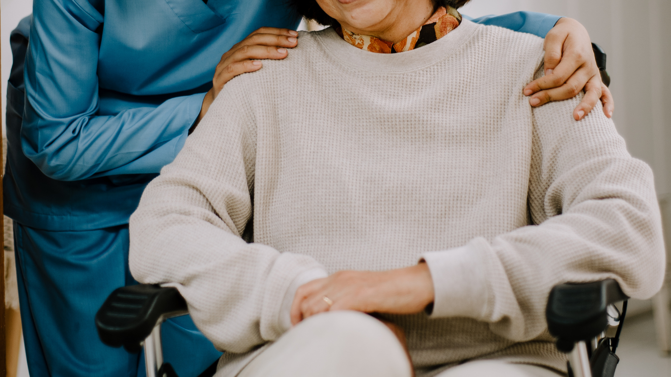 Una pareja de ancianos desempacando compras cerca de una ventana; un hombre sostiene un teléfono y una mujer mete la mano en una bolsa verde.