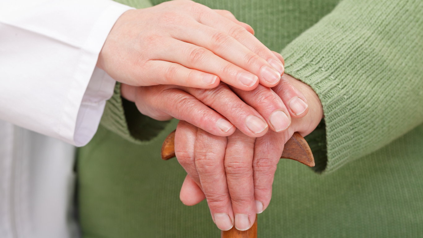 Cuatro adultos mayores y un cuidador sentados en un sofá en una sala de estar; el cuidador está sonriendo.