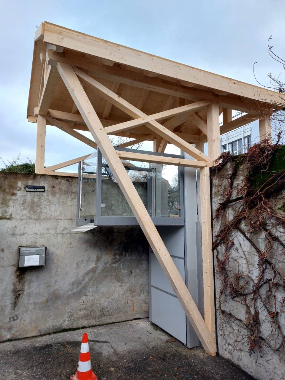 Auvent en bois et structure de support au-dessus d'un ascenseur vertical devant un mur en béton.