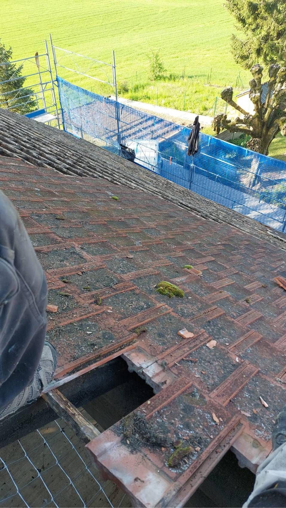 Couvreur travaillant sur un toit de tuiles rouges abîmé par les intempéries.