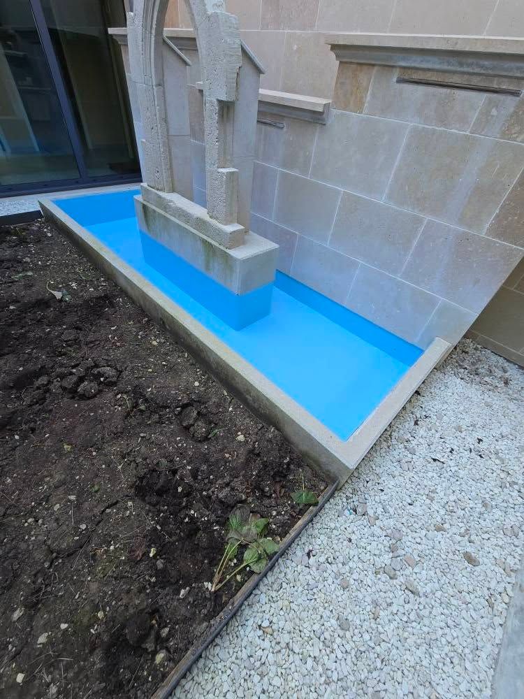 Revêtement de protection bleu autour du soubassement d’un bâtiment en pierre, le long d’un chemin de terre et d’une allée en gravier