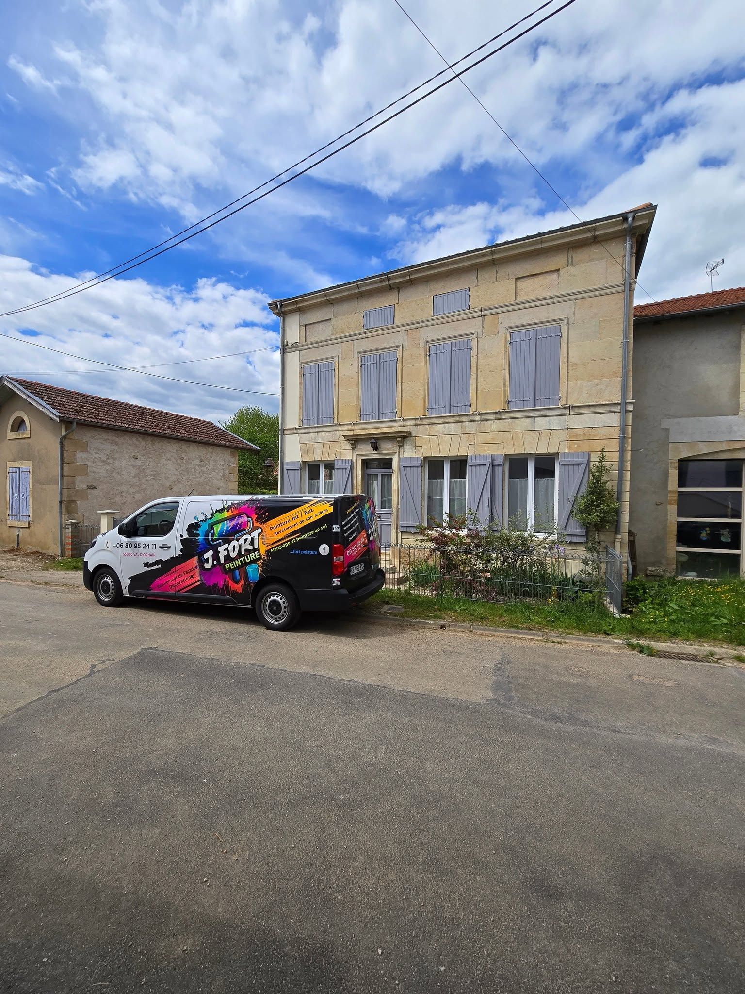 Maison beige à deux étages, aux fenêtres condamnées, avec une camionnette de service colorée garée devant sous un ciel nuageux