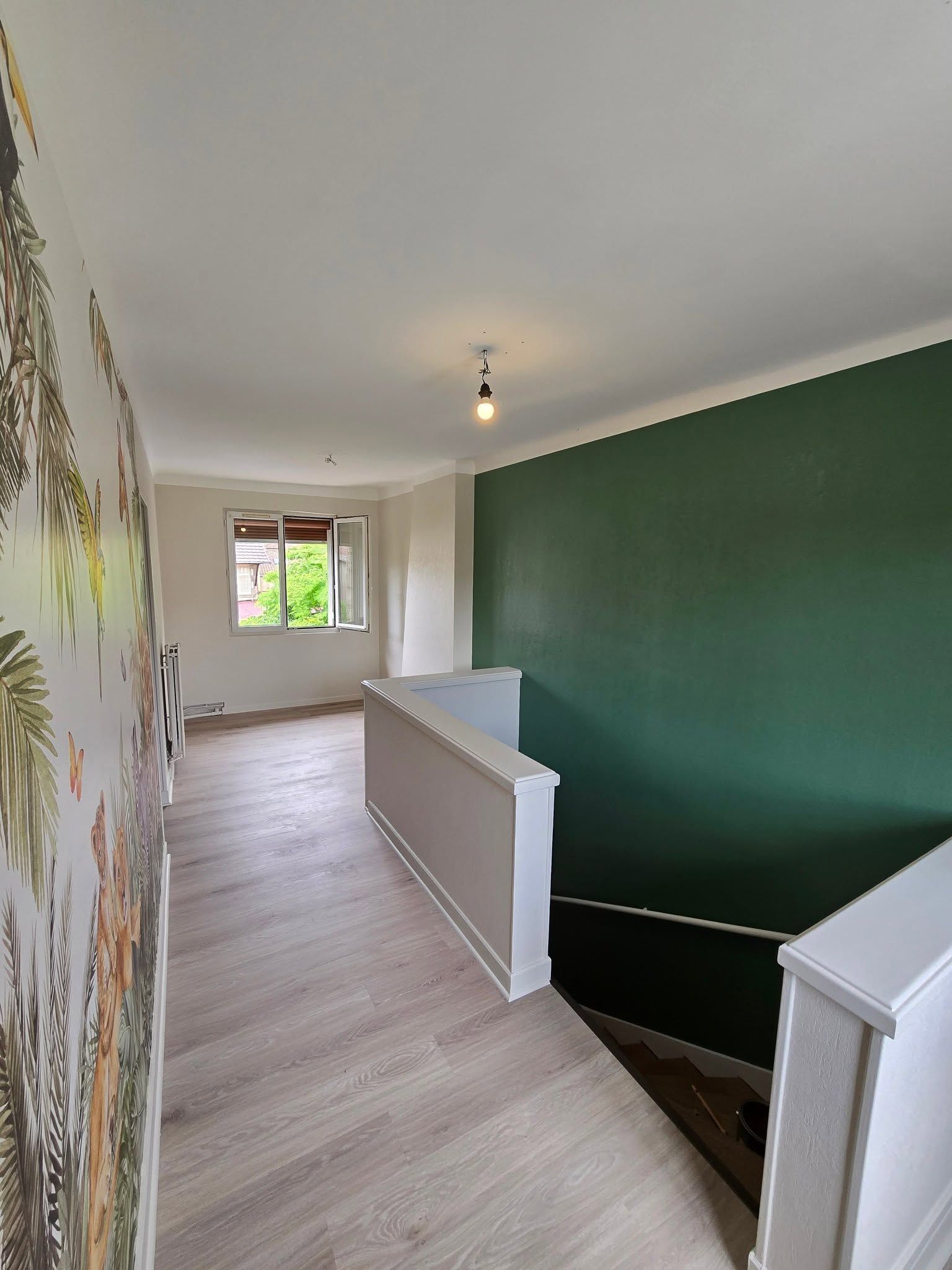 Palier lumineux avec un mur d’accent vert, une rampe blanche, un parquet clair et une fenêtre au fond