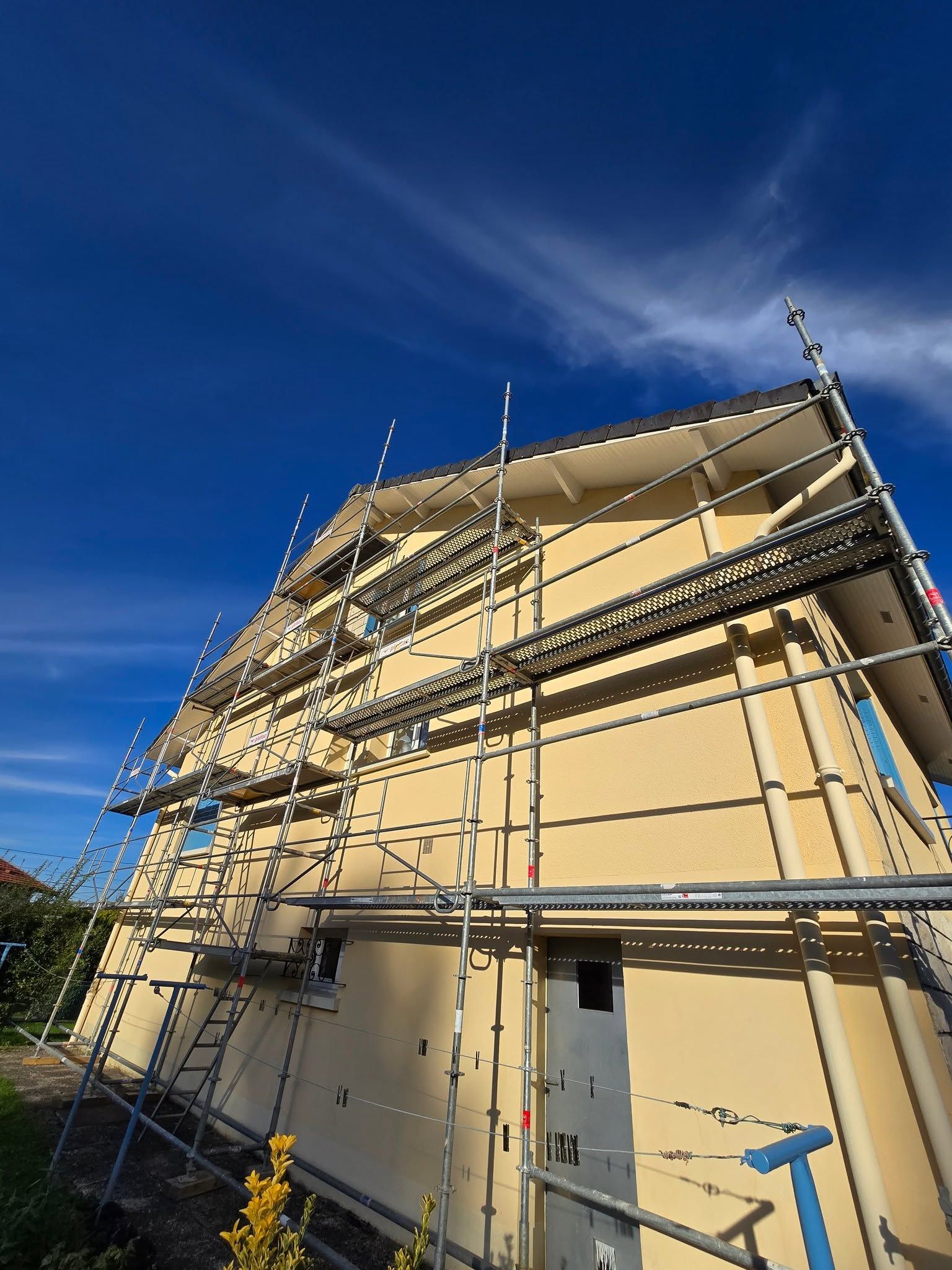 Échafaudage autour d’une maison beige sous un ciel bleu éclatant