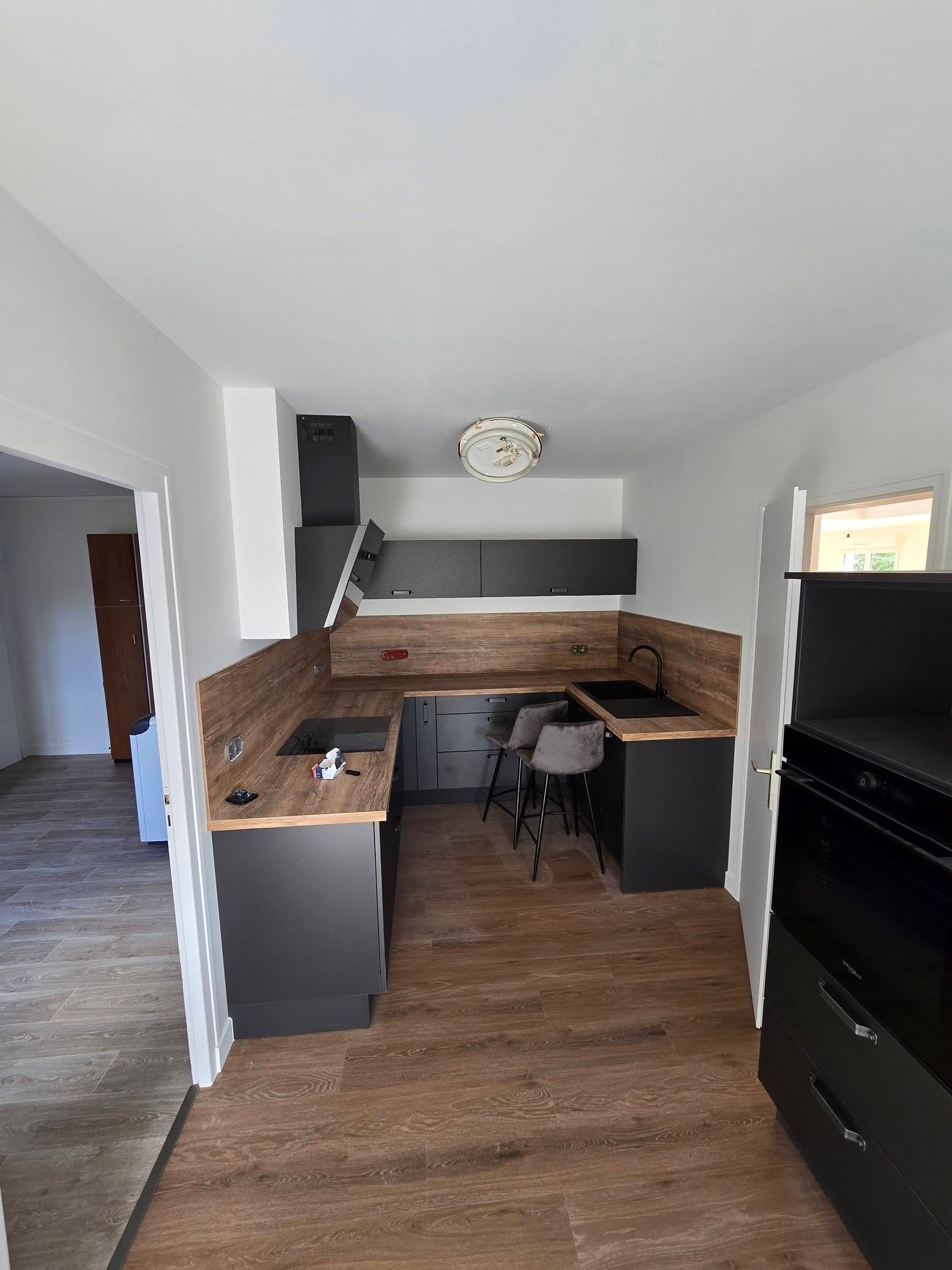 Petite cuisine moderne avec des placards sombres, des plans de travail en bois et une chaise de salle à manger noire sous les placards hauts.