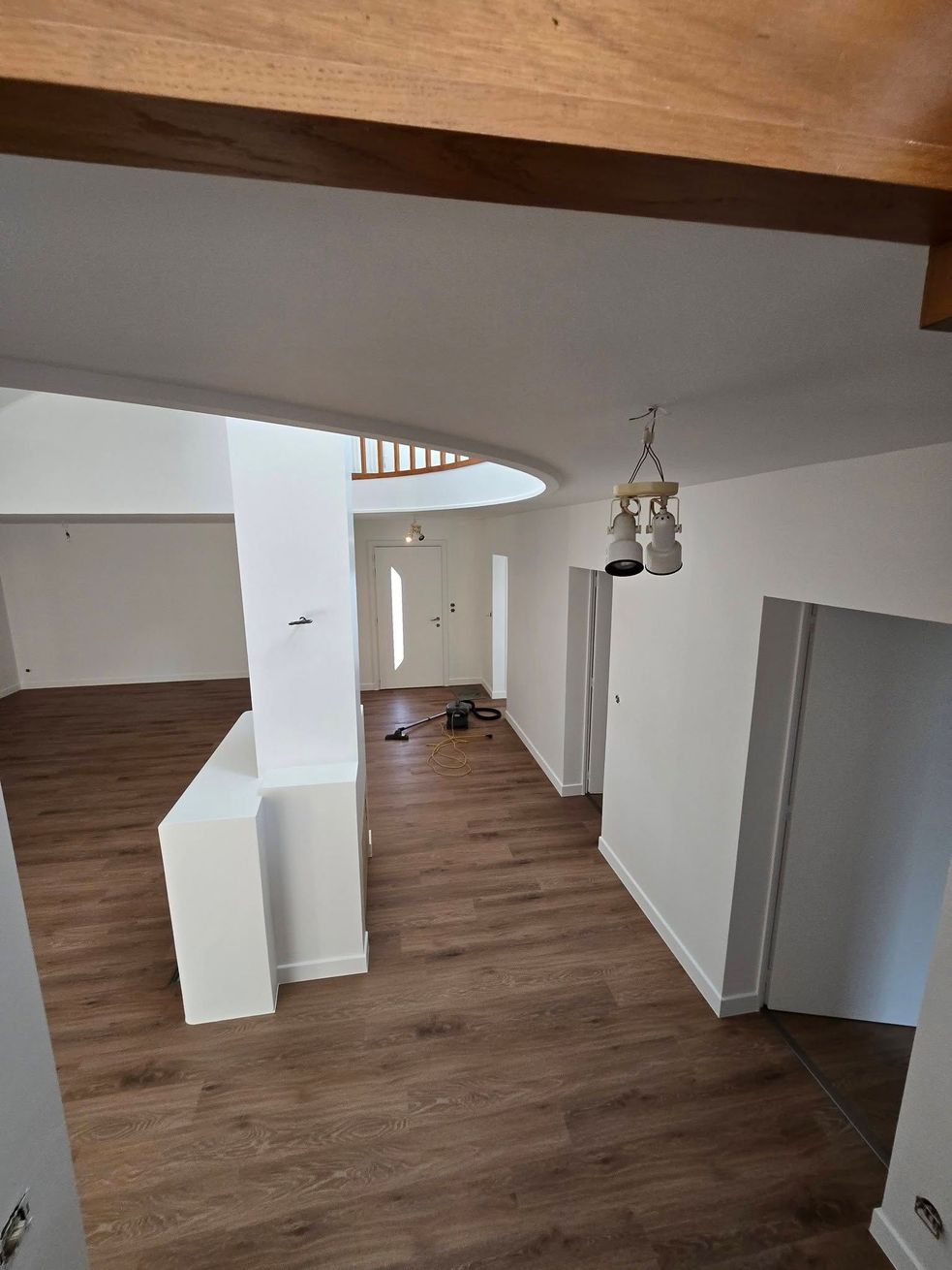 Intérieur de loft moderne et vide, avec parquet, murs blancs, ouverture cintrée dans le plafond et suspension lumineuse