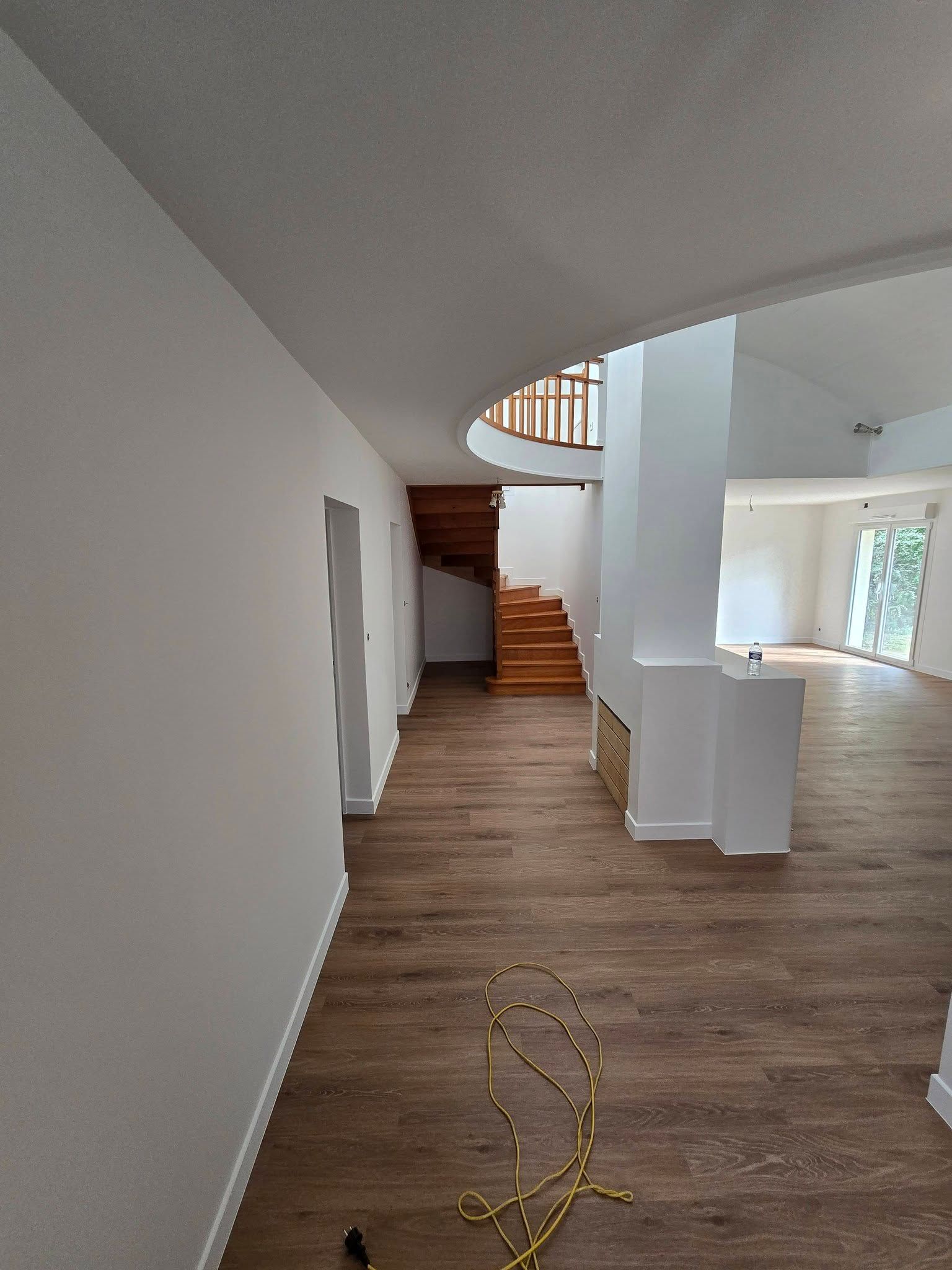 Couloir vide avec un parquet, des murs blancs, un escalier et un cordon jaune au sol