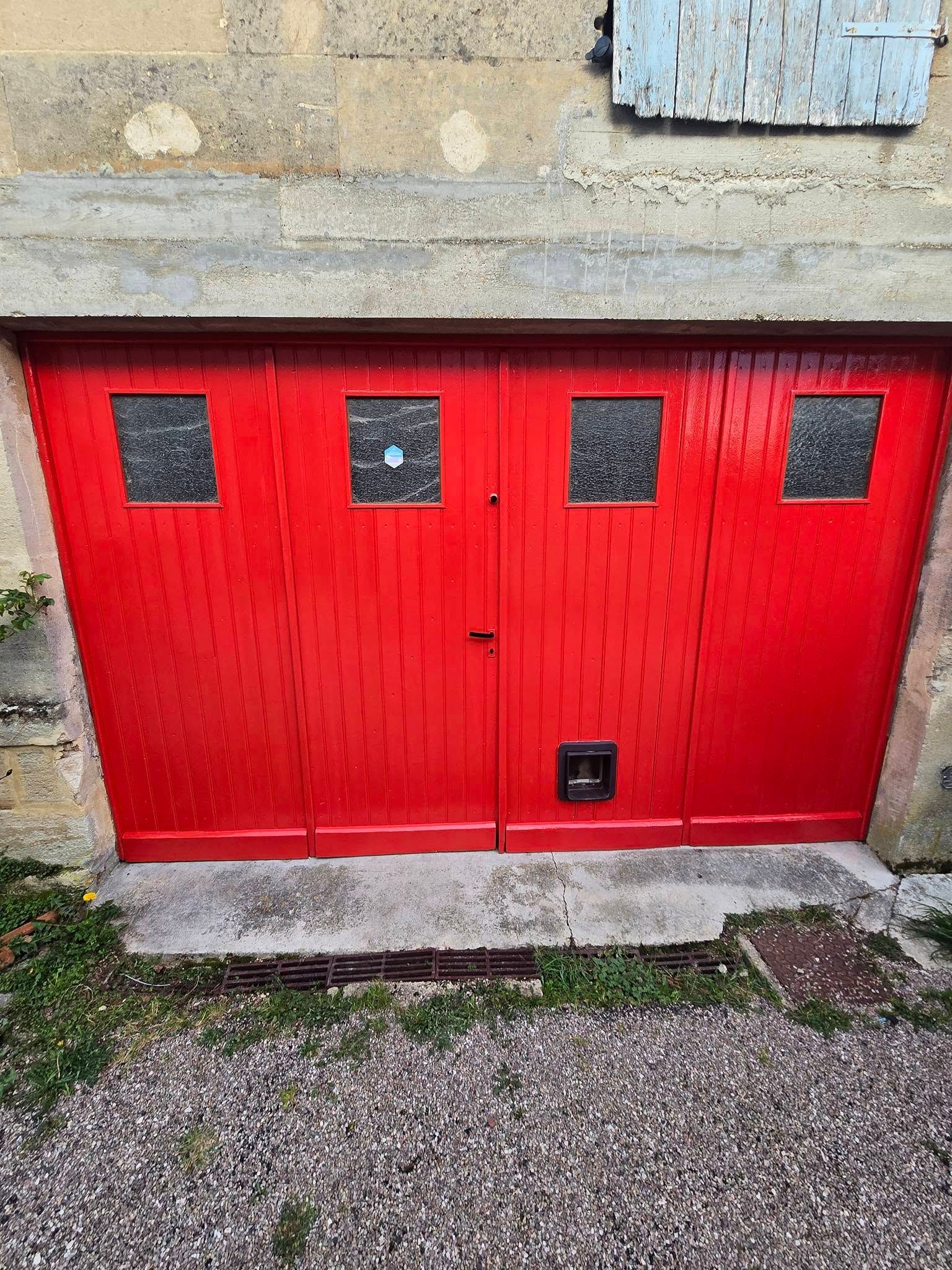 Portes de garage doubles rouge vif avec quatre petites fenêtres sous un mur de pierre.