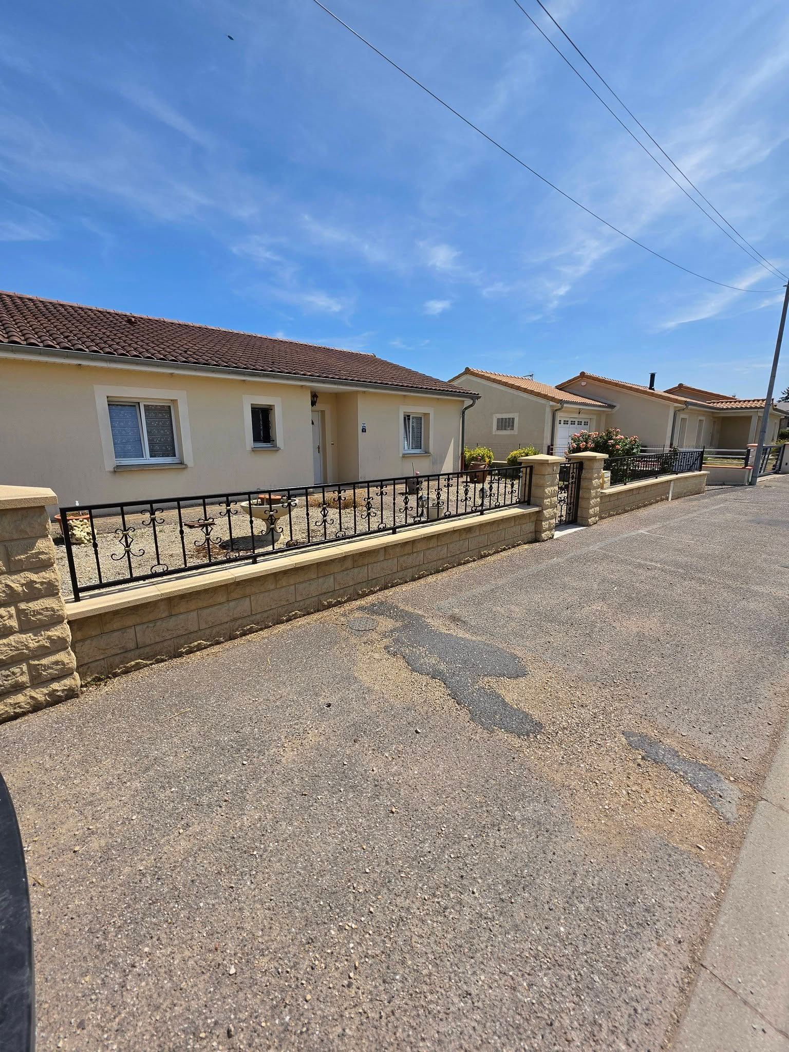 Rue résidentielle calme bordée de maisons de plain-pied, de murets en pierre et baignée par un ciel bleu dégagé