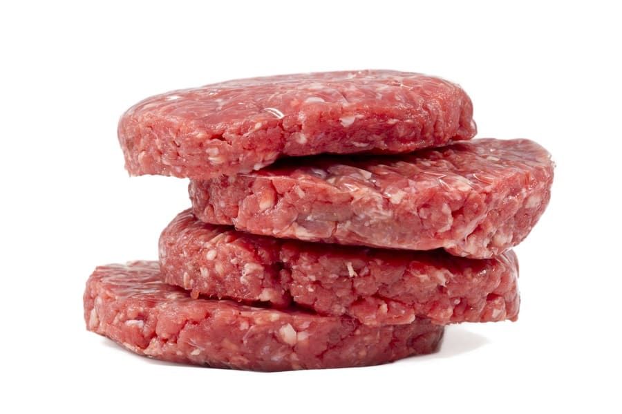Tres hamburguesas crudas se apilan una encima de otra sobre un fondo blanco.