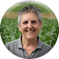 Eine Frau lächelt vor einem Feld grüner Pflanzen.