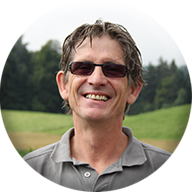 Ein Mann mit Sonnenbrille und grauem Hemd lächelt in einem Kreis.