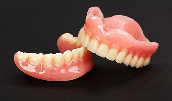 Dos dentaduras postizas removibles de color rosa y blanco sobre un fondo negro.