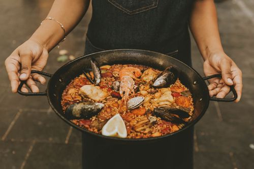 Tres platos de arroz con mariscos sobre una mesa de madera, incluyendo paella y risotto.