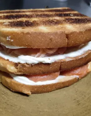 Sándwich tostado con mantequilla blanca y relleno en rodajas sobre un plato marrón.