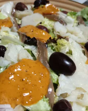 Ensalada con queso blanco, aceitunas y aderezo de naranja en un plato.