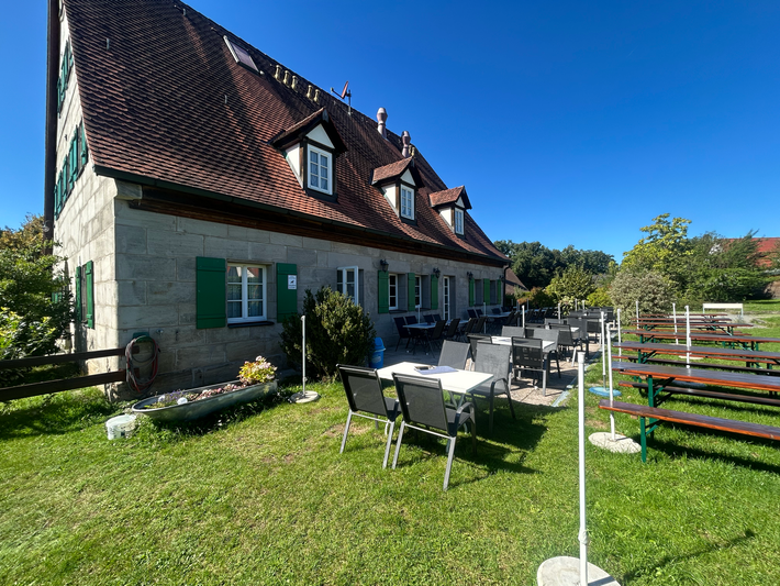 Tische im Restaurant im Freien mit Tellern, Gläsern und Besteck. Rustikale Holztische und dunkle Stühle.