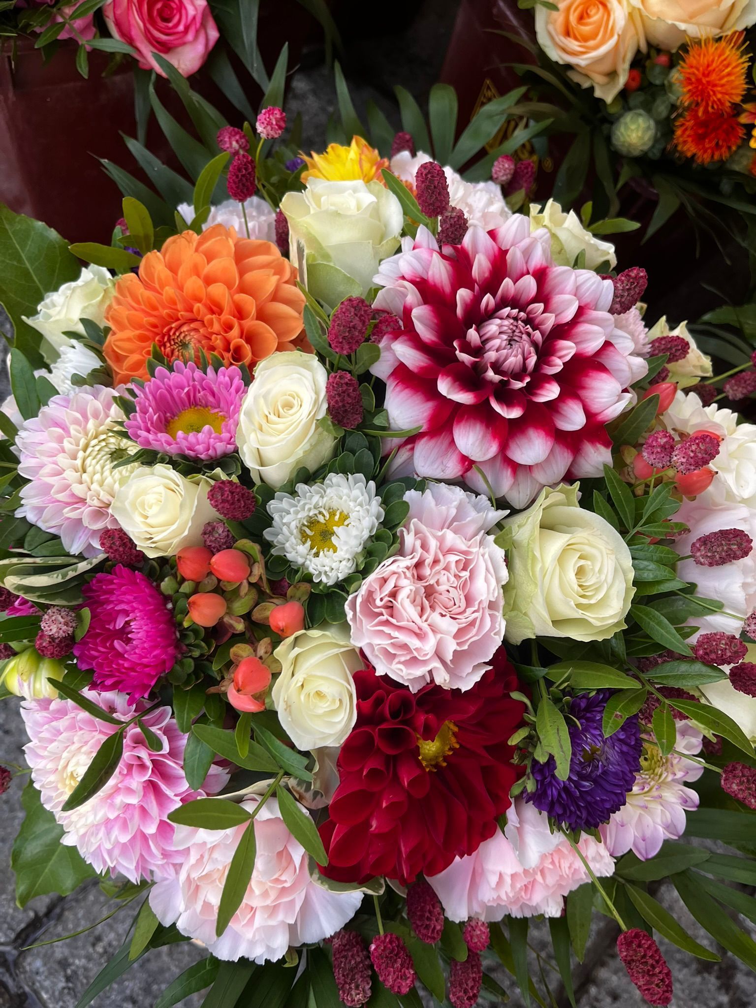Nahaufnahme eines farbenfrohen Blumenstraußes mit Dahlien, Rosen und Nelken in verschiedenen Rosa-, Orange- und Rottönen.
