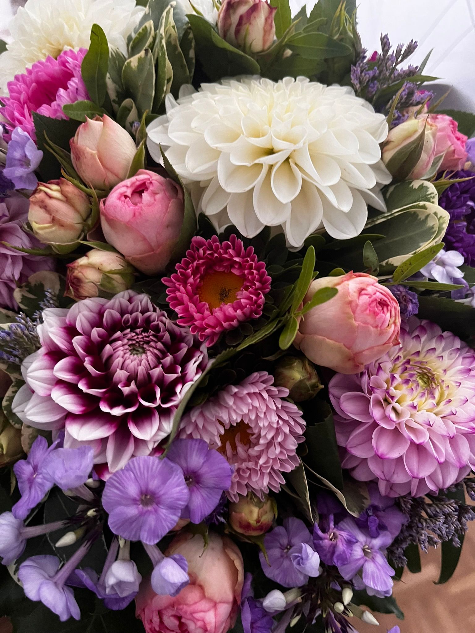 Nahaufnahme eines farbenfrohen Blumenarrangements: Dahlien, Rosen und Lavendelblüten in Rosa-, Lila- und Weißtönen.