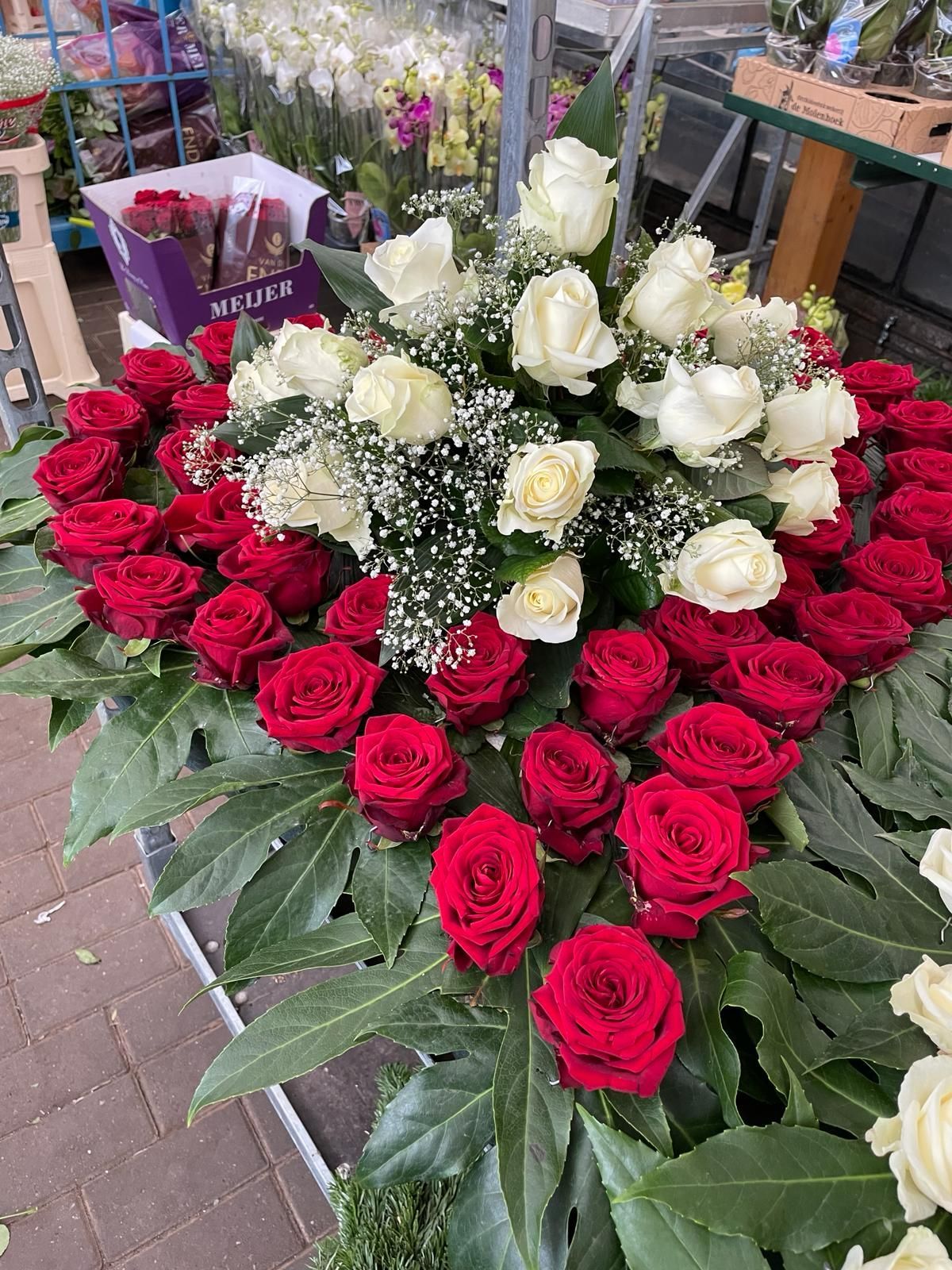 Herzförmiges Blumenarrangement aus roten und weißen Rosen mit grünem Beiwerk auf einem Tisch.