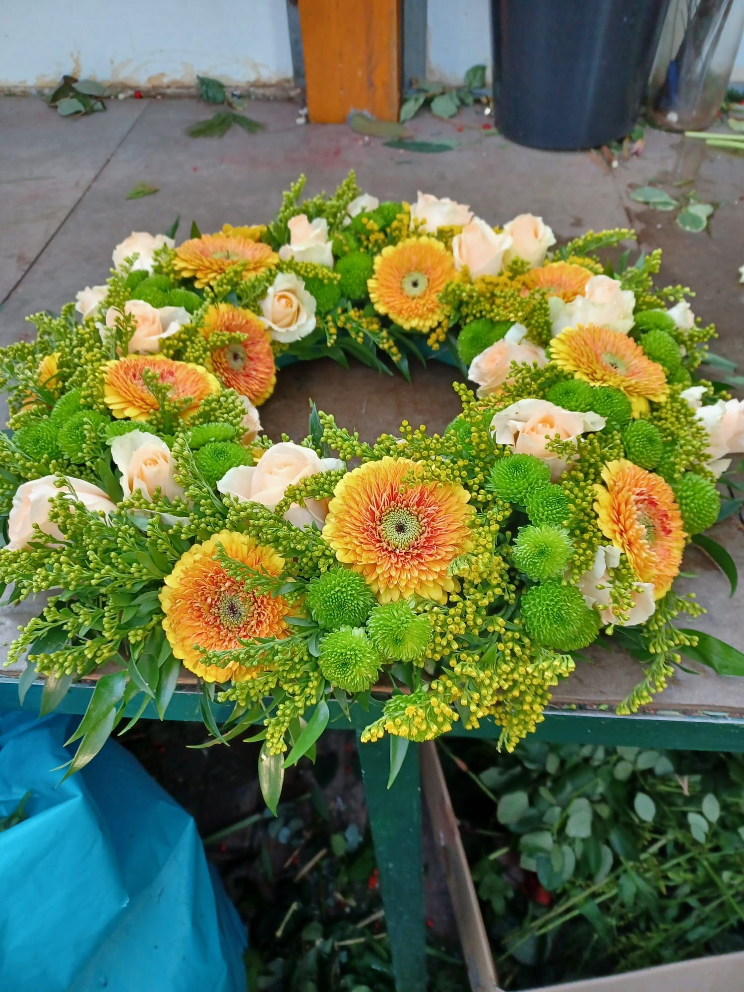 Blumenkranz mit orangefarbenen Gerbera-Gänseblümchen, weißen Rosen und grünen Akzenten.