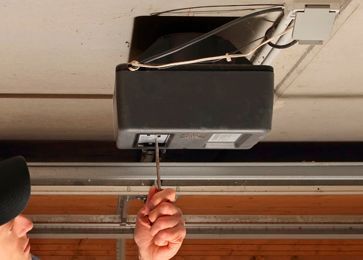 Un hombre está arreglando un abridor de puerta de garaje con un destornillador.