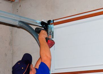 Un hombre está instalando una puerta de garaje con un taladro.
