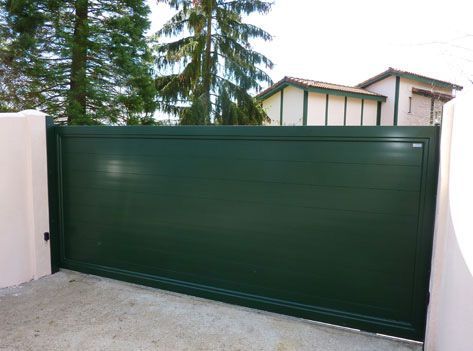 Una puerta corrediza verde con una casa al fondo.