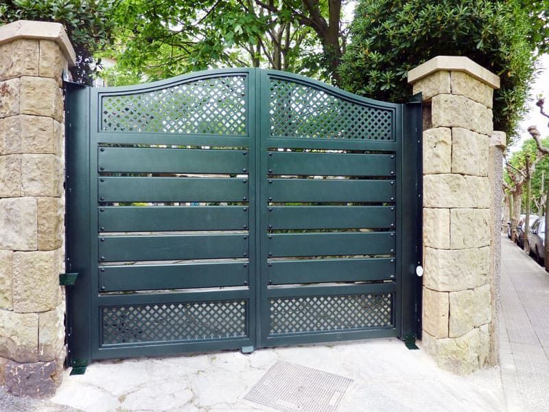 Una puerta verde está rodeada de pilares de piedra y árboles.