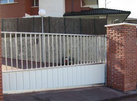 Una puerta blanca se abre a un camino de entrada al lado de una pared de ladrillos.