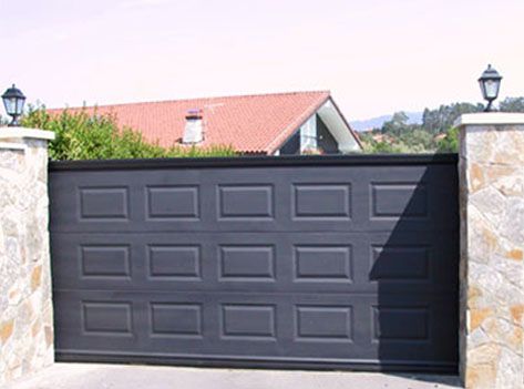 Una puerta de garaje negra está abierta frente a una casa.