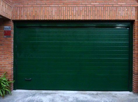 Una puerta de garaje verde está delante de un edificio de ladrillos.