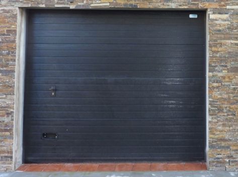 Una puerta de garaje negra con una pared de piedra detrás.