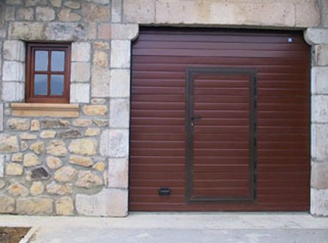 Una puerta de garaje marrón está junto a una pared de piedra con una ventana.