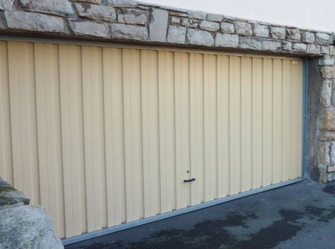 Una puerta de garaje de color beige está junto a una pared de piedra.