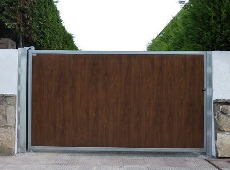 Una puerta de madera con marco de metal se abre a un camino de entrada.