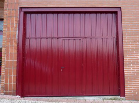 Una puerta de garaje roja con una pared de ladrillos detrás.