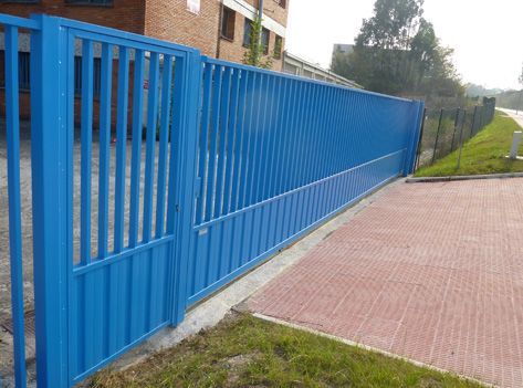 Una valla metálica azul rodea un camino de entrada de ladrillo.