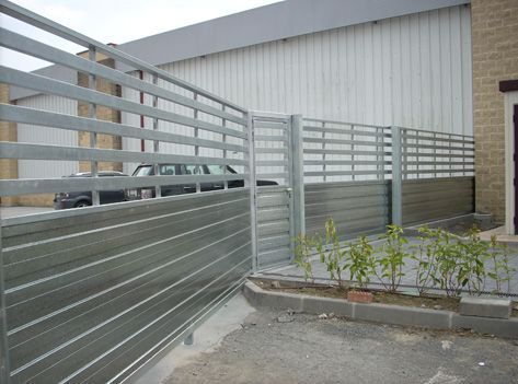 Una valla metálica rodea un aparcamiento delante de un edificio.