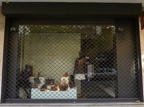 Un escaparate con una valla alrededor y el reflejo de una persona en el escaparate.