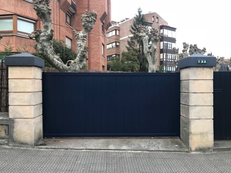 Una puerta corrediza azul está rodeada de pilares de piedra frente a un edificio de ladrillo.
