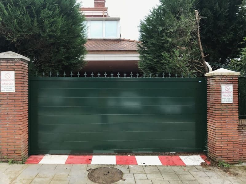 Una puerta verde está rodeada de pilares de ladrillo y árboles.
